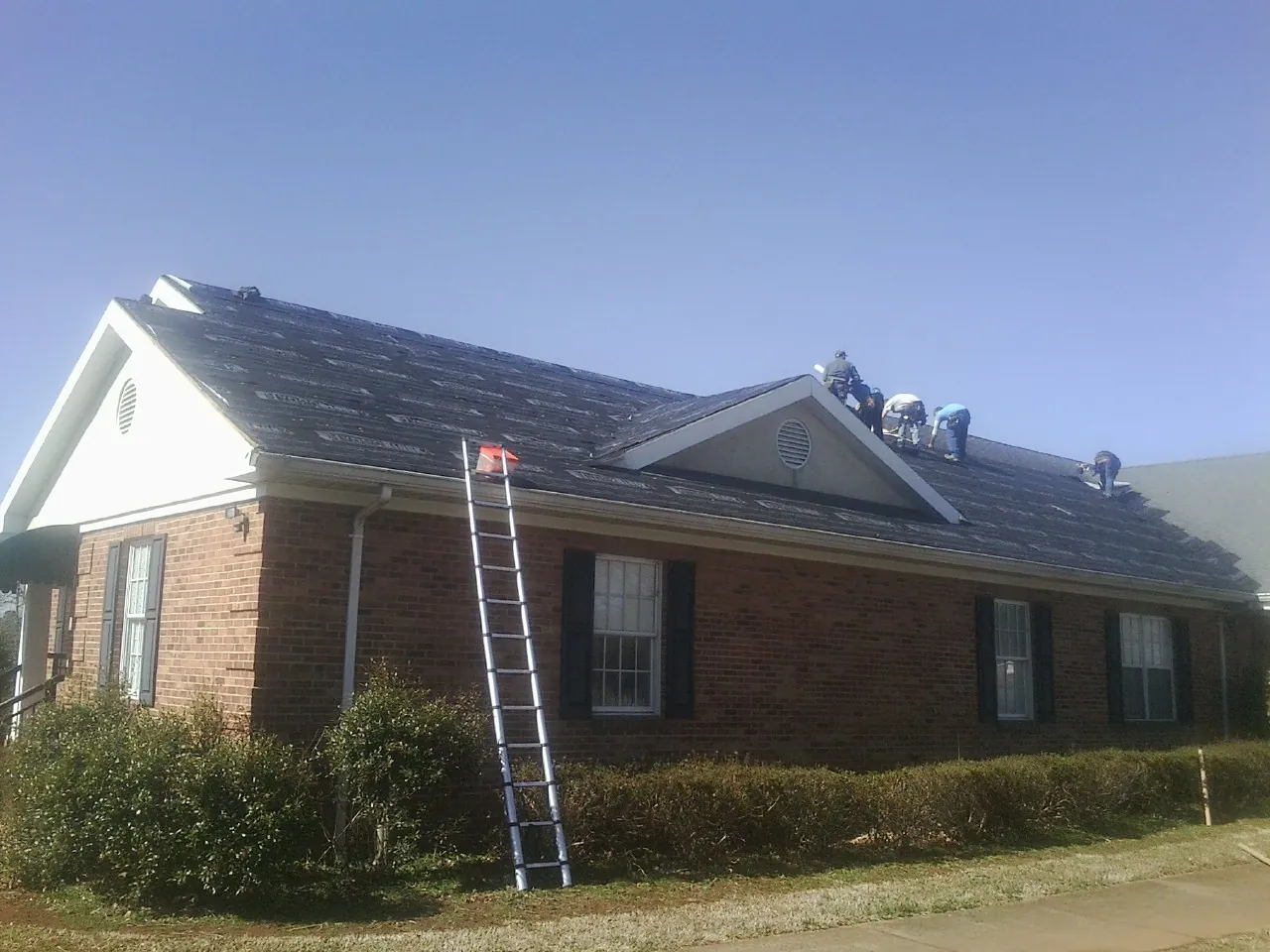 Crew tearing shingles off a brick ranch roof with a ladder set — Metal Roof Repair work by our crew in Lake Elmo