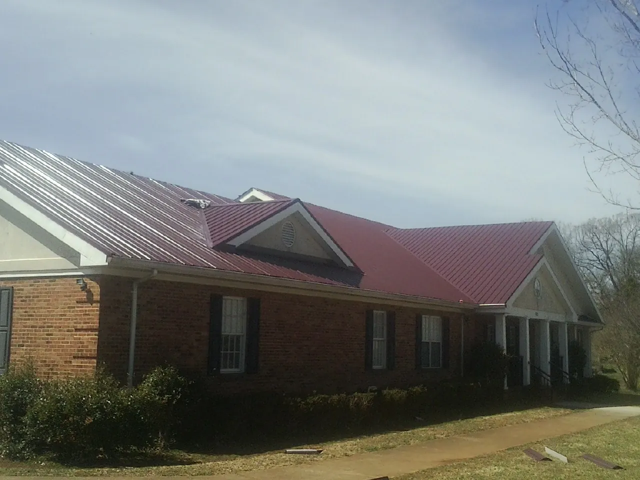 Red metal roof with gabled entries on a long brick building, from a Hail Damage Roof Repair job in Lake Elmo