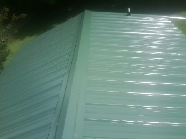 New green metal panels meeting at the ridge of a roof — Flat Roof Repair work by our crew in Lake Elmo