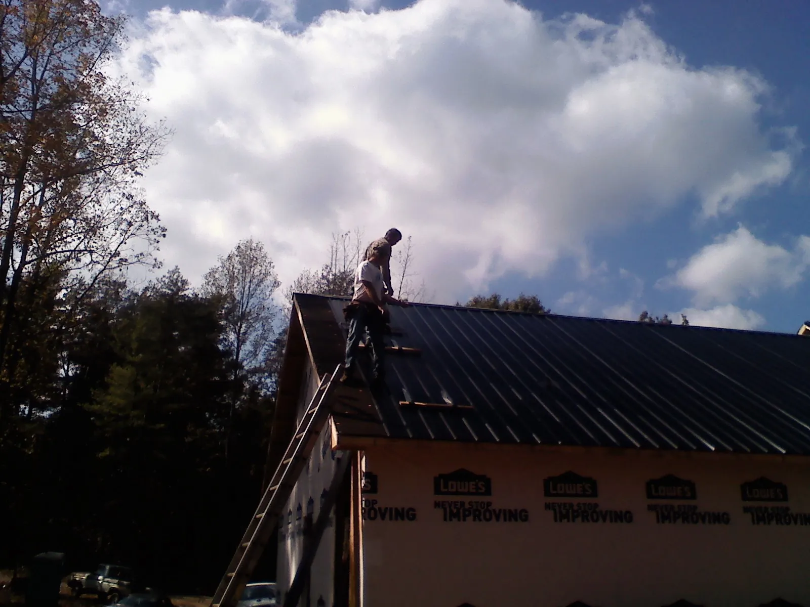Roofer fastening dark metal panels high against a cloudy sky, from a Roof Inspection job in Lake Elmo