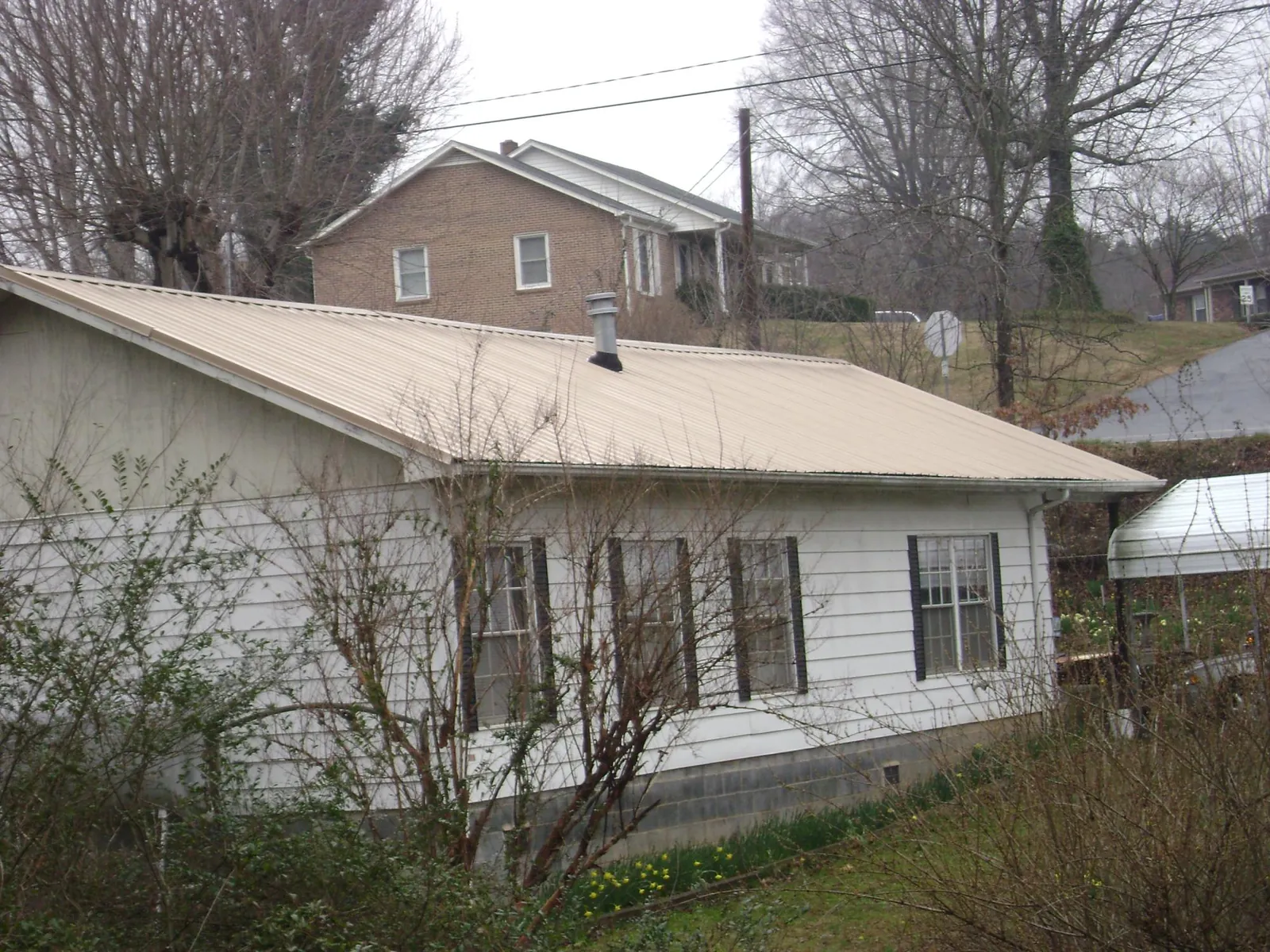 Tan metal roof on a white sided house set into a hillside — Commercial Roofing by Roofing Brothers in Lake Elmo
